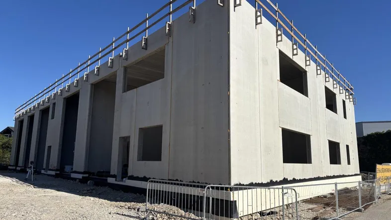 Rohbau eines modernen Geschäftsgebäudes mit Betonwänden und Fensteröffnungen unter blauem Himmel.