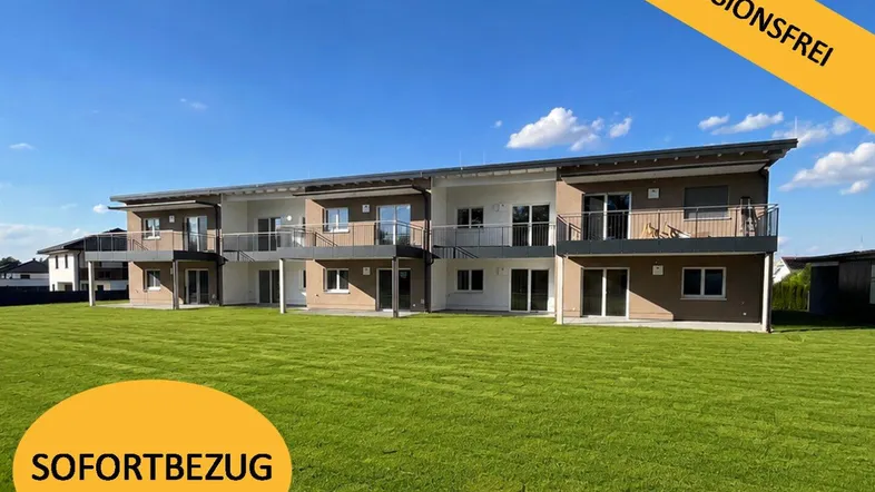 Moderne Reihenhausanlage mit großzügiger Rasenfläche und Balkonen unter blauem Himmel.