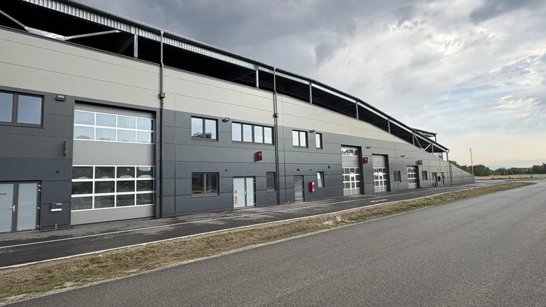 Modernes Industriegebäude mit mehreren Garagentoren und Fenstern unter bewölktem Himmel.