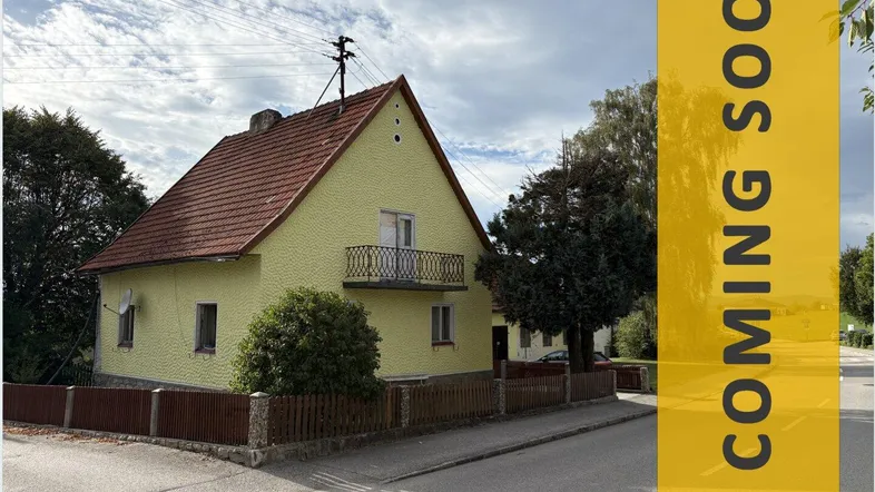 Gelbes Einfamilienhaus mit Satteldach, kleinem Balkon und ländlicher Umgebung an einer Straße.