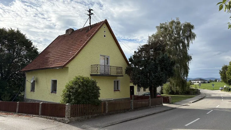 Gelbes Einfamilienhaus mit rotem Ziegeldach und kleinem Balkon an einer Landstraße.
