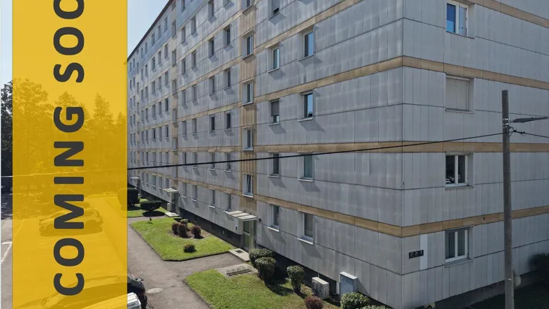 Mehrstöckiges Wohngebäude mit grauer Fassade und umliegenden Grünflächen, bereit für die Vermarktung.