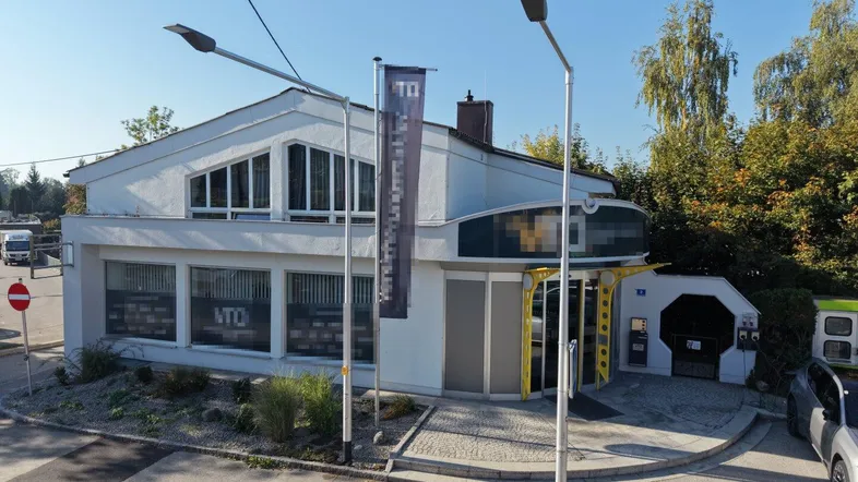 Modernes Geschäftsgebäude mit großen Fenstern und gepflegter Außenanlage an einer Straße gelegen.