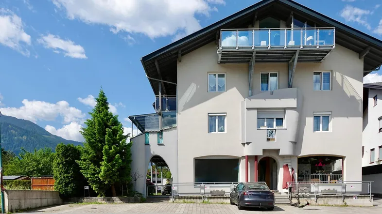 Mehrstöckiges Gebäude mit modernen Balkonen und Bergblick unter blauem Himmel.