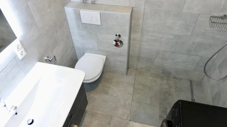 Modernes Badezimmer mit grauen Fliesen, wandhängendem WC, Waschbecken und ebenerdiger Dusche.