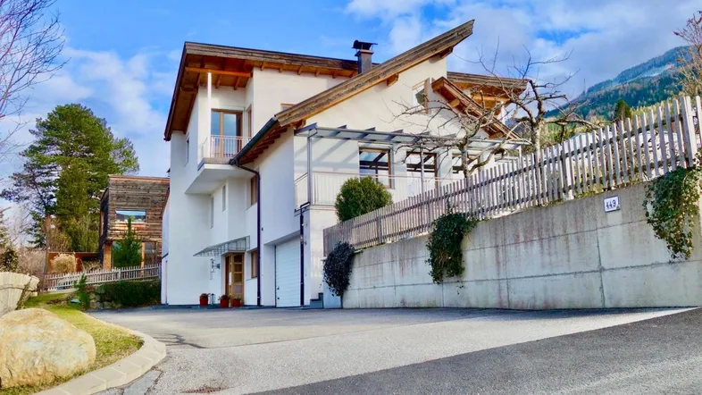 Modernes Wohnhaus mit weißer Fassade, Holzelementen und Garagenzufahrt in bergiger Umgebung.