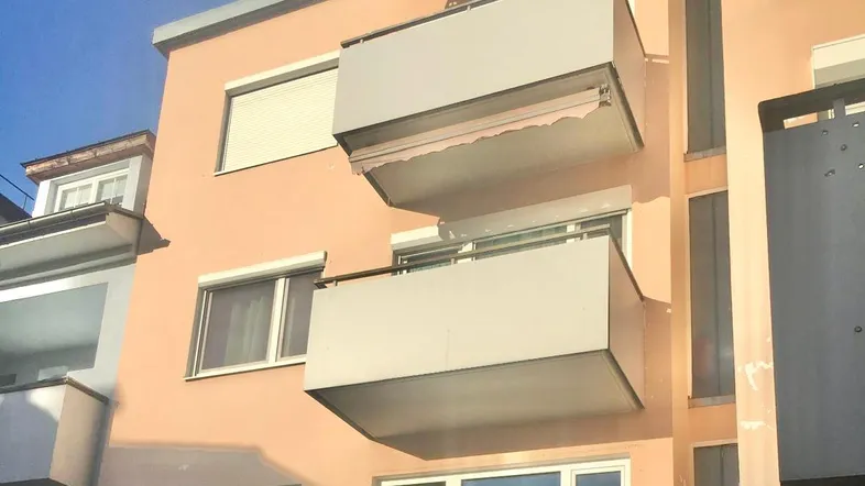 Fassade eines Wohngebäudes mit mehreren Balkonen und Rollläden an den Fenstern.
