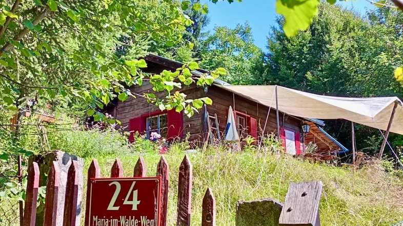 Rustikales Holzhaus mit roten Fensterläden, umgeben von üppigem Grün und einem Wegweiser.