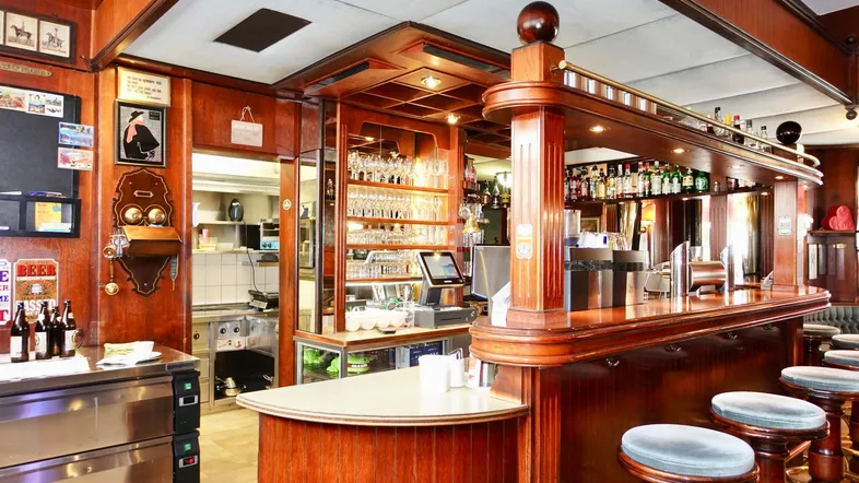 Eine traditionelle Bar mit dunklem Holz, Barhockern und einer gut bestückten Theke, die zum Verweilen einlädt.