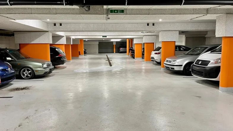 Geräumige Tiefgarage mit zahlreichen Stellplätzen, orangefarbenen Säulen und sichtbaren Installationen.