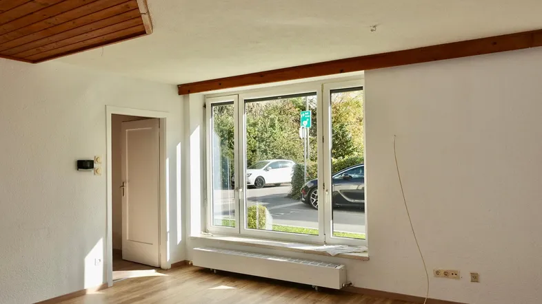 Heller Wohnraum mit Laminatboden, großen Fenstern und Holzbalken an der Decke.