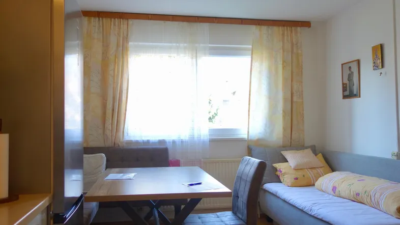 Kleiner, heller Wohn- und Essbereich mit Esstisch, Sitzbank und Tagesbett am Fenster.