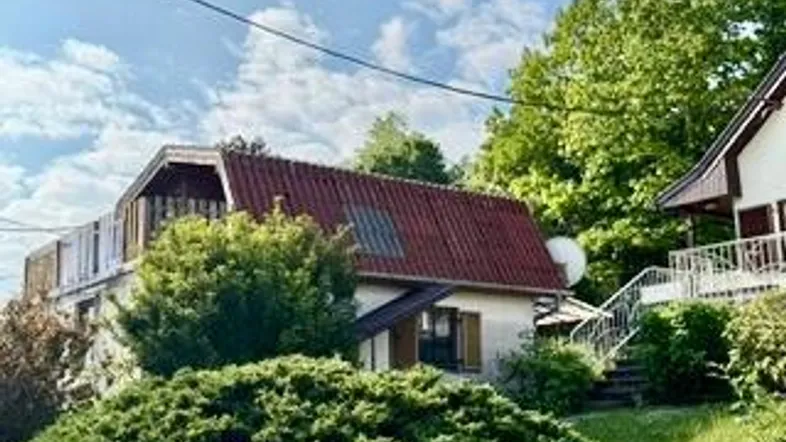 Haus mit rotem Satteldach und üppiger grüner Bepflanzung in einer natürlichen Umgebung.