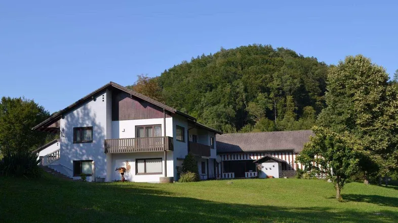 Charmantes Landhaus mit Balkonen und Satteldach, eingebettet in eine grüne Hügellandschaft.