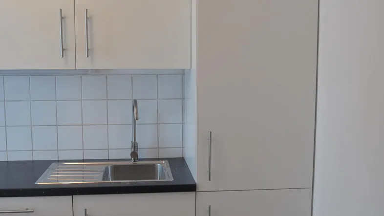 Moderne Küche mit weißen Schränken, dunkler Arbeitsplatte, Spüle und gefliestem Spritzschutz.