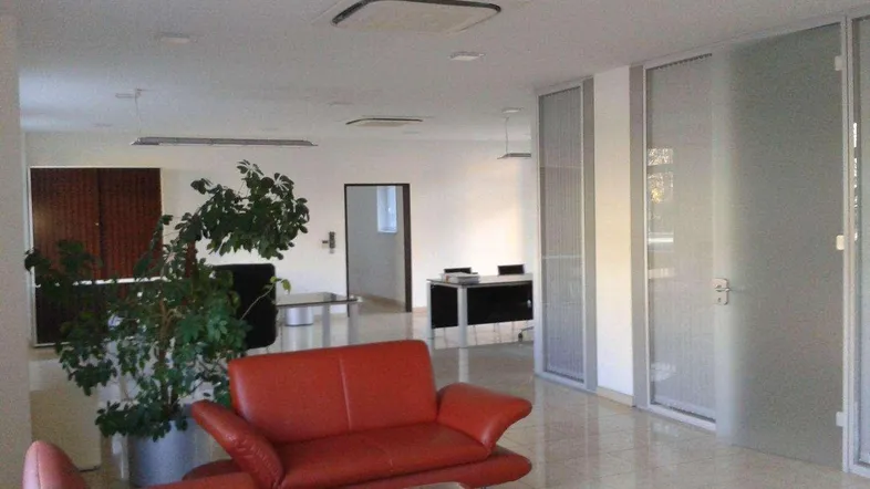 Geräumiger Bürobereich mit rotem Sofa, Glastisch und modernen Trennwänden für eine offene Arbeitsumgebung.