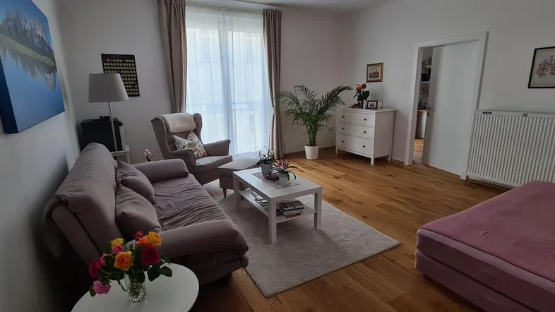 Helles Wohnzimmer mit Holzboden, bequemen Sofas und Zugang zu einem Balkon oder einer Terrasse.