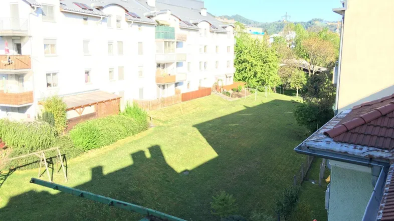 Blick von einem Balkon auf einen großen, gepflegten Gemeinschaftsgarten mit Rasenfläche und Spielgeräten.