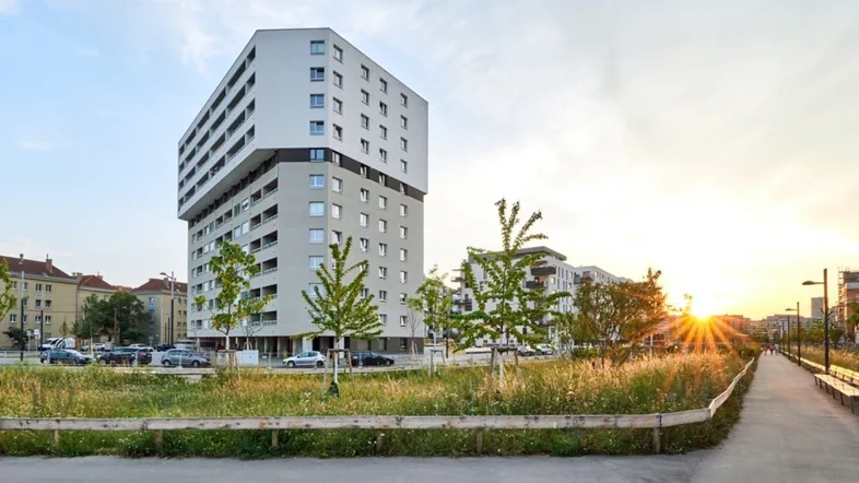 Modernes Wohngebäude bei Sonnenuntergang mit Grünflächen und Spazierweg in urbaner Umgebung.