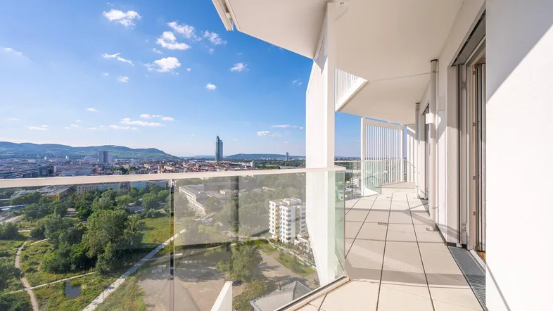 Langer, sonniger Balkon mit Glasbrüstung und weitem Blick über die Stadt und die umliegende Landschaft.