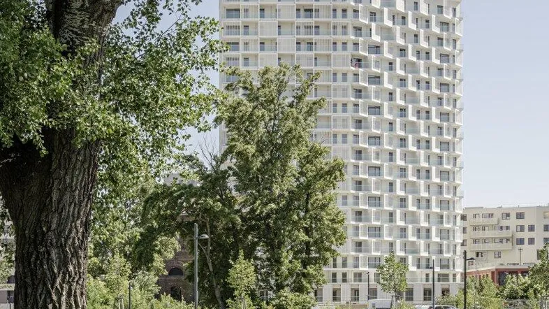 Hohes, modernes Wohngebäude mit vielen Balkonen, umgeben von grüner Parklandschaft und Bäumen.