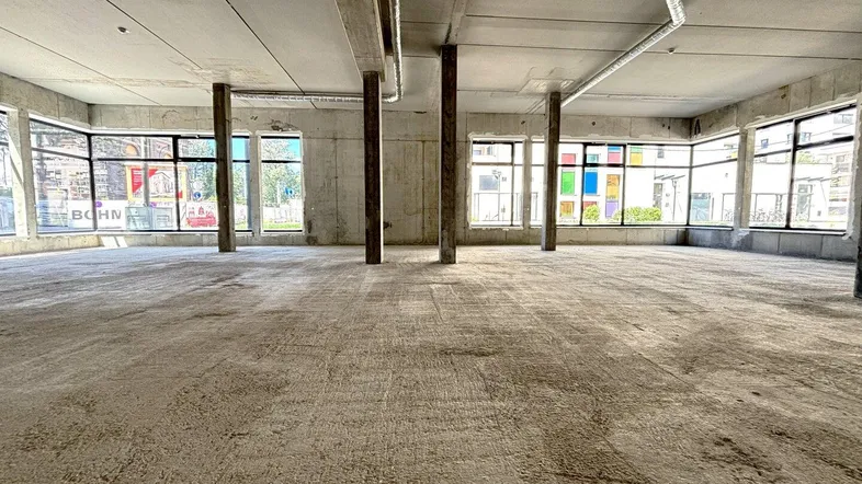 Großer, unfertiger Gewerberaum mit Betonboden und vielen Fenstern, bereit für den zukünftigen Ausbau.