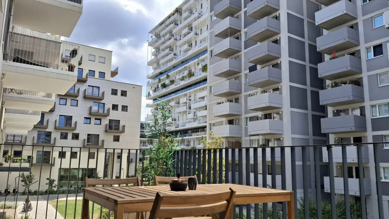 Geräumiger Balkon mit Holztisch und Stühlen, bietet Blick auf den begrünten Innenhof und moderne Gebäude.