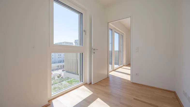 Heller Raum mit Holzboden und großen Fenstern, die viel Tageslicht hereinlassen.
