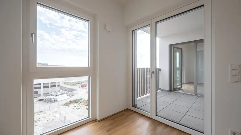 Helles Zimmer mit Parkettboden und Zugang zu einem Balkon, bietet einen weiten Blick.