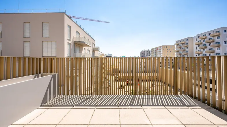 Geräumige Terrasse mit Holzzaun und Blick auf die umliegenden Gebäude unter blauem Himmel.