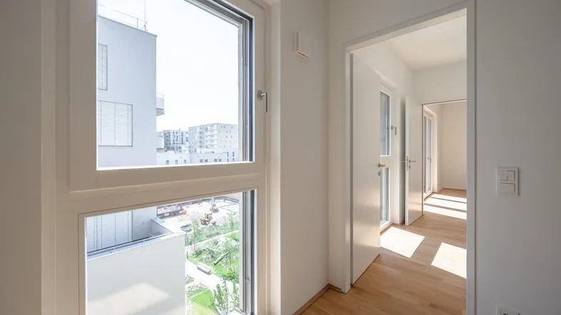 Heller Flur mit Parkettboden und großem Fenster, das viel Tageslicht hereinlässt.
