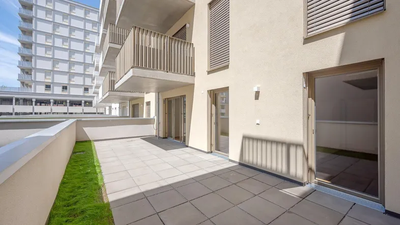 Geräumige Terrasse mit Steinplatten und Grünstreifen, ideal für entspannte Stunden im Freien.