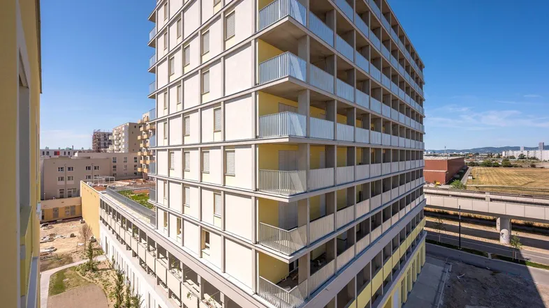Modernes Apartmentgebäude mit zahlreichen Balkonen und Blick auf die Umgebung unter blauem Himmel.