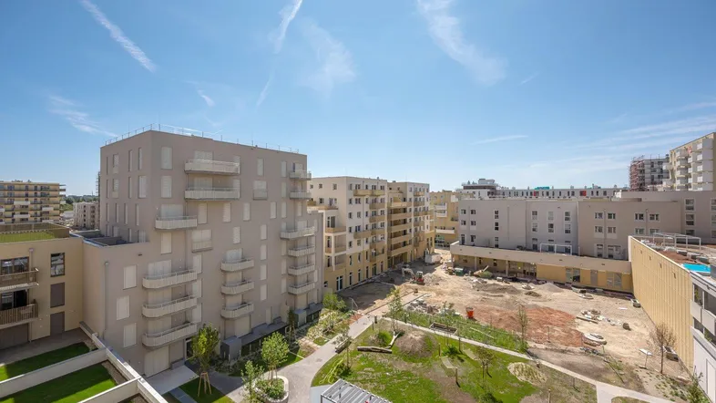 Überblick über eine moderne Wohnanlage mit mehreren Gebäuden, Grünflächen und Baustellen unter blauem Himmel.