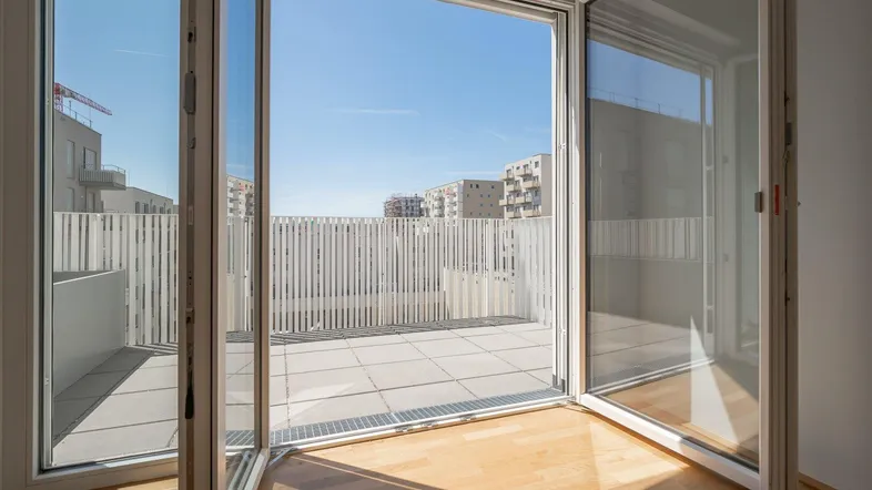 Helles Zimmer mit großen Glasfronten und direktem Zugang zu einer weitläufigen Terrasse mit Stadtblick.