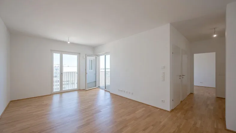 Helles, leeres Wohnzimmer mit Parkettboden und Zugang zu zwei Balkonen, ideal für individuelle Gestaltung.