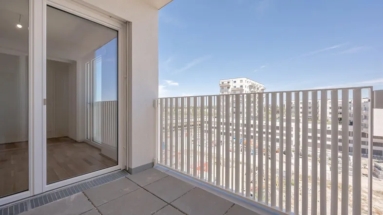 Heller Balkon mit Fliesenboden und Blick auf die umliegenden Neubauten unter blauem Himmel.