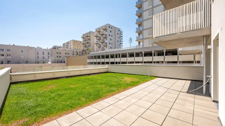 Große Terrasse mit Rasenfläche und Blick auf moderne Wohngebäude.