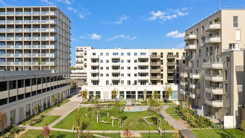 Weitläufiger Gemeinschaftsgarten mit Spielbereichen und modernen Wohngebäuden unter blauem Himmel.