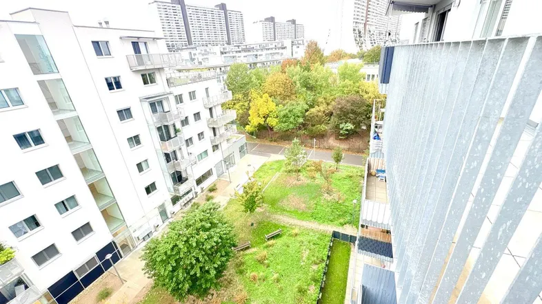 Blick von einem Balkon auf den begrünten Innenhof und umliegende moderne Wohngebäude.