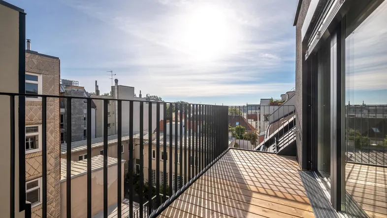 Moderner Balkon mit Holzbelag und schwarzem Metallgeländer, bietet einen Blick auf die Stadt.