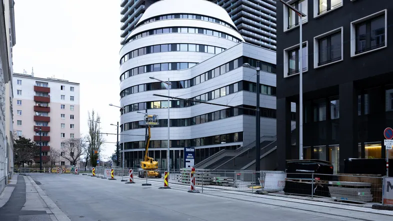 Moderne Gebäude mit geschwungener Fassade und Baustelle an einer städtischen Straße.