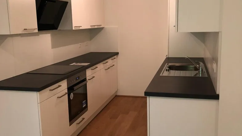 Moderne Einbauküche mit weißen Schränken, dunkler Arbeitsplatte und integrierten Geräten, ideal für effizientes Kochen.