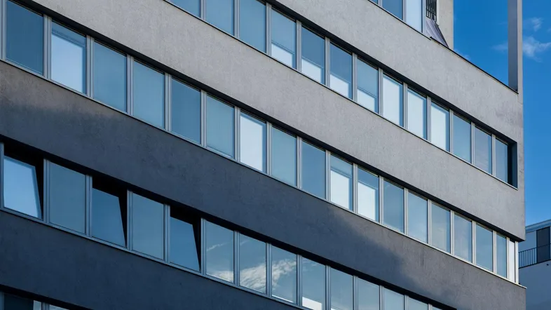 Moderne Fassade eines Bürogebäudes mit vielen reflektierenden Fenstern unter blauem Himmel.