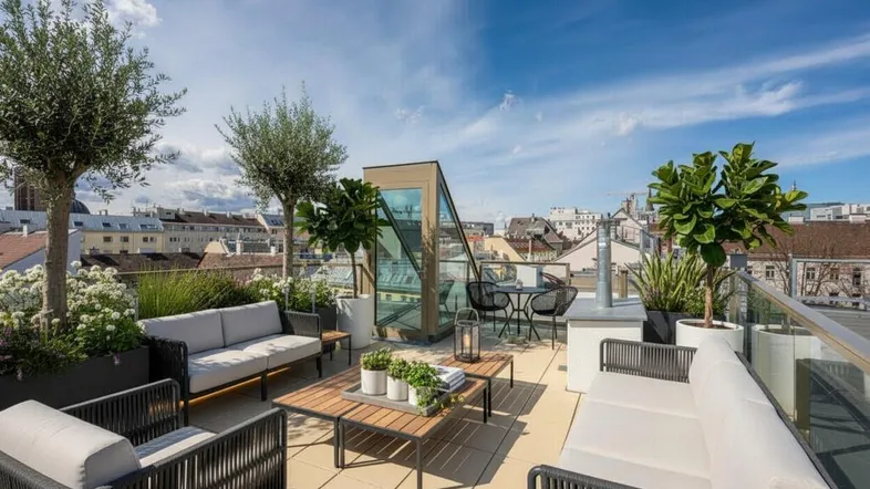 Geräumige Dachterrasse mit bequemen Loungemöbeln, Pflanzen und weitem Stadtblick unter blauem Himmel.