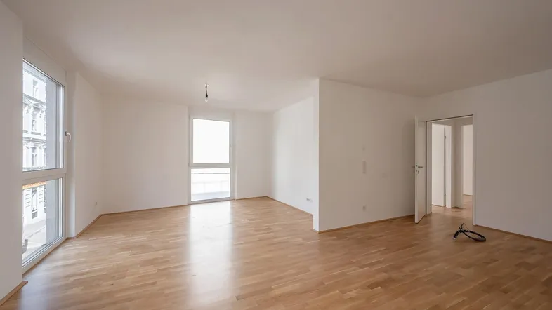 Helles, leeres Zimmer mit Parkettboden und großen Fenstern, bereit für die individuelle Gestaltung.