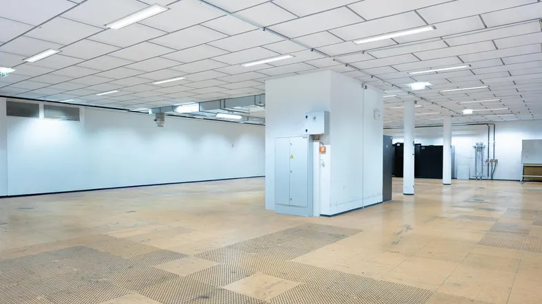 Großer, leerer Gewerberaum mit hellen Wänden, abgehängter Decke und funktionaler Beleuchtung, ideal für Büros oder Lager.