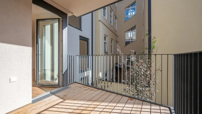Heller Balkon mit Holzboden und Blick auf den Innenhof des Gebäudes.