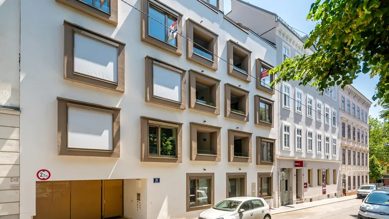 Moderne Wohnhausfassade mit quadratischen Fenstern und Tiefgaragenzufahrt an einer Stadtstraße.