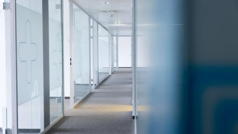Langer Bürogang mit Glaswänden und Teppichboden, der zu weiteren Büroräumen führt.